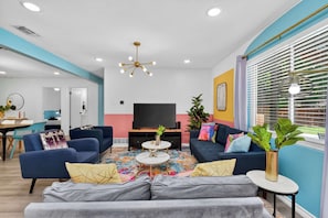 A modern living room with a TV, sofas, a coffee table, and a dining area. - Modern NRH Retreat | Pool, BBQ & Sleeps 10 (Fort Worth)