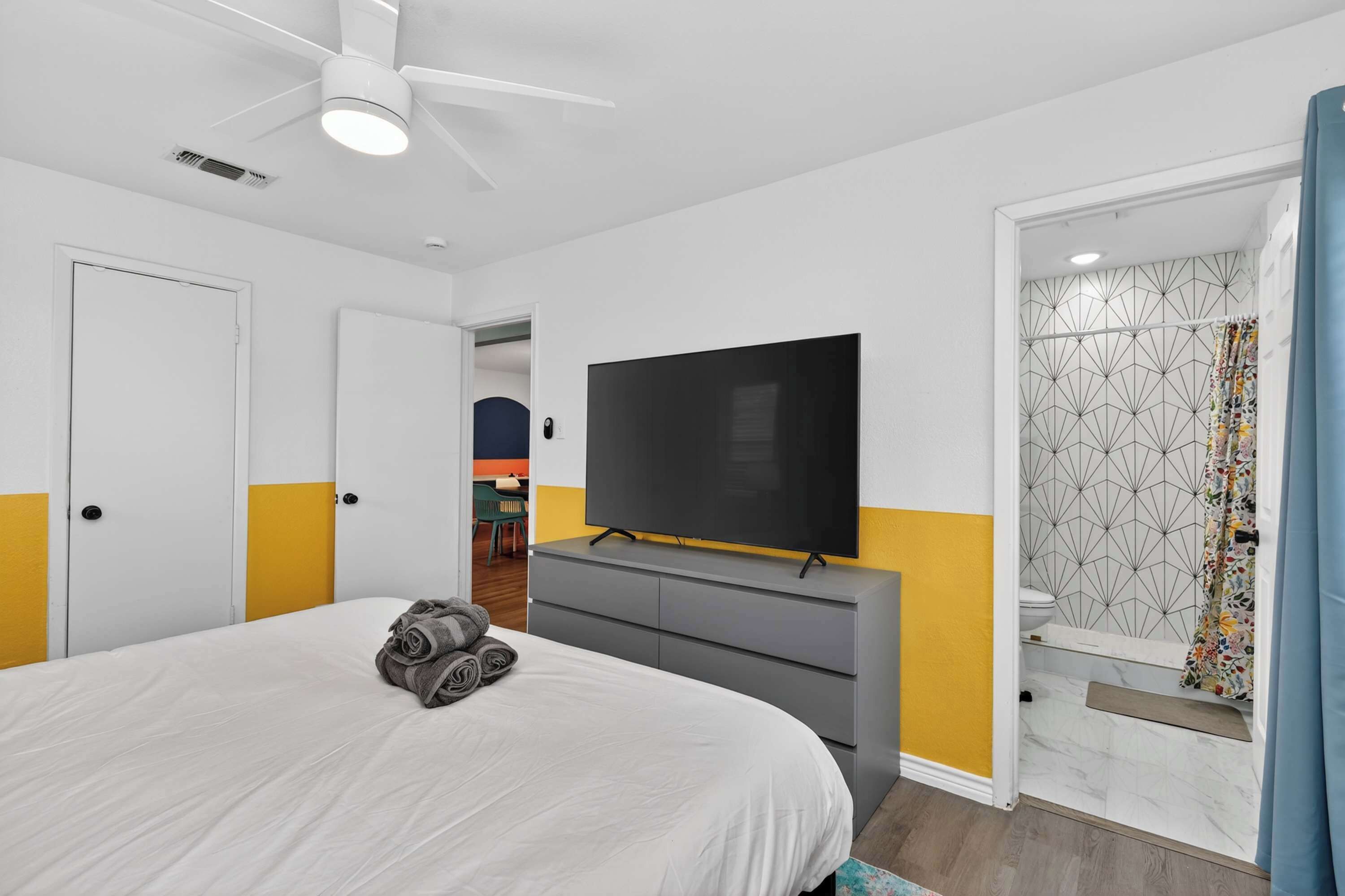 Ein Hotelzimmer mit Bett, Flachbildfernseher, Deckenventilator und Badezimmer mit Duschvorhang.