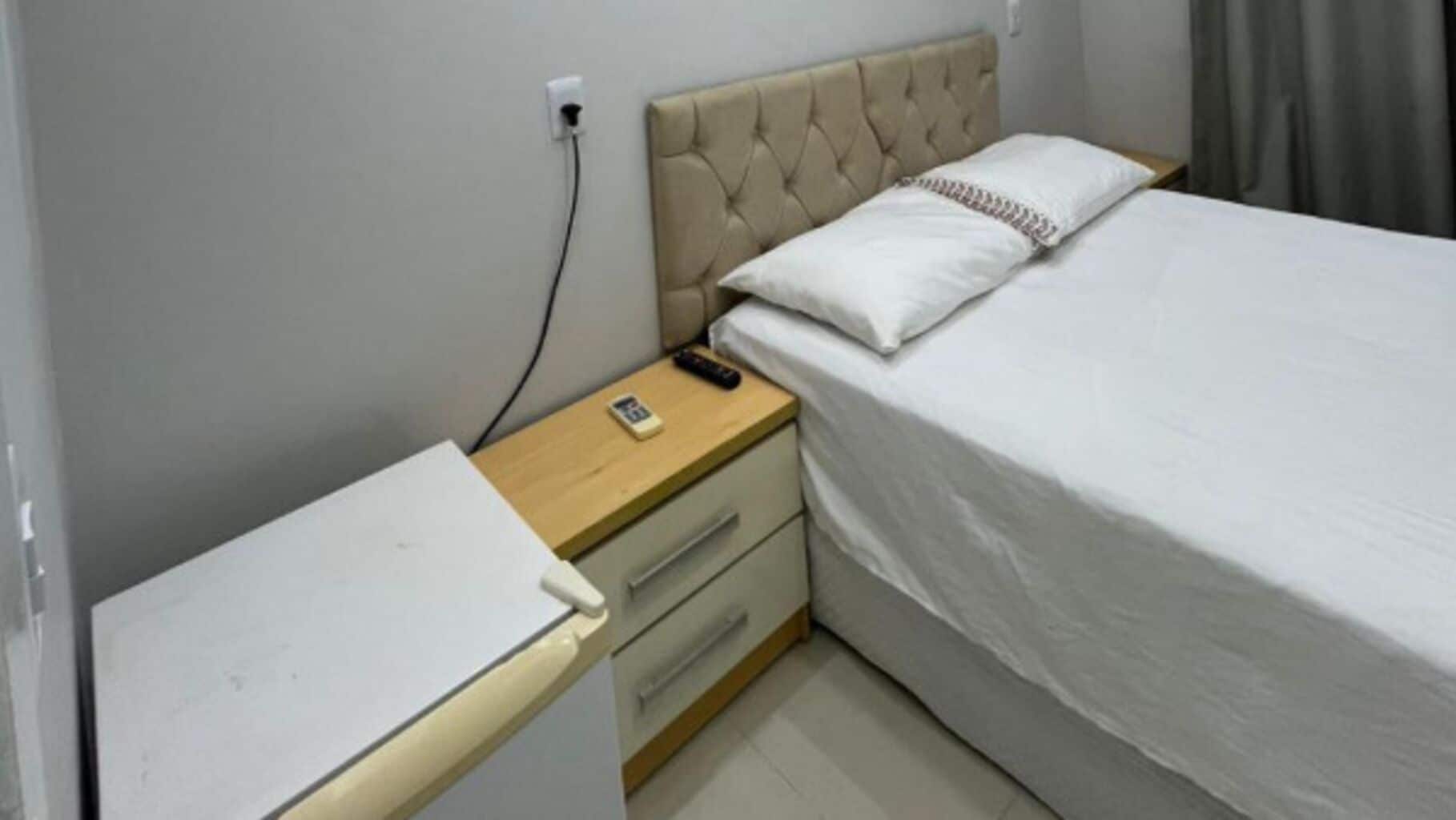 Un dormitorio pequeño con una cama, una mesita de noche, un mueble con cajones y un enchufe.