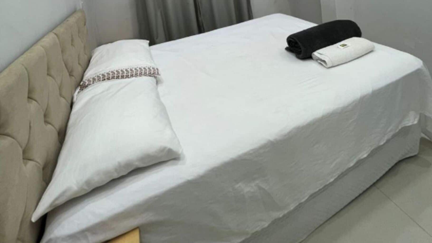 Una cama bien tendida con edredón blanco, una toalla negra y un cojín decorativo.