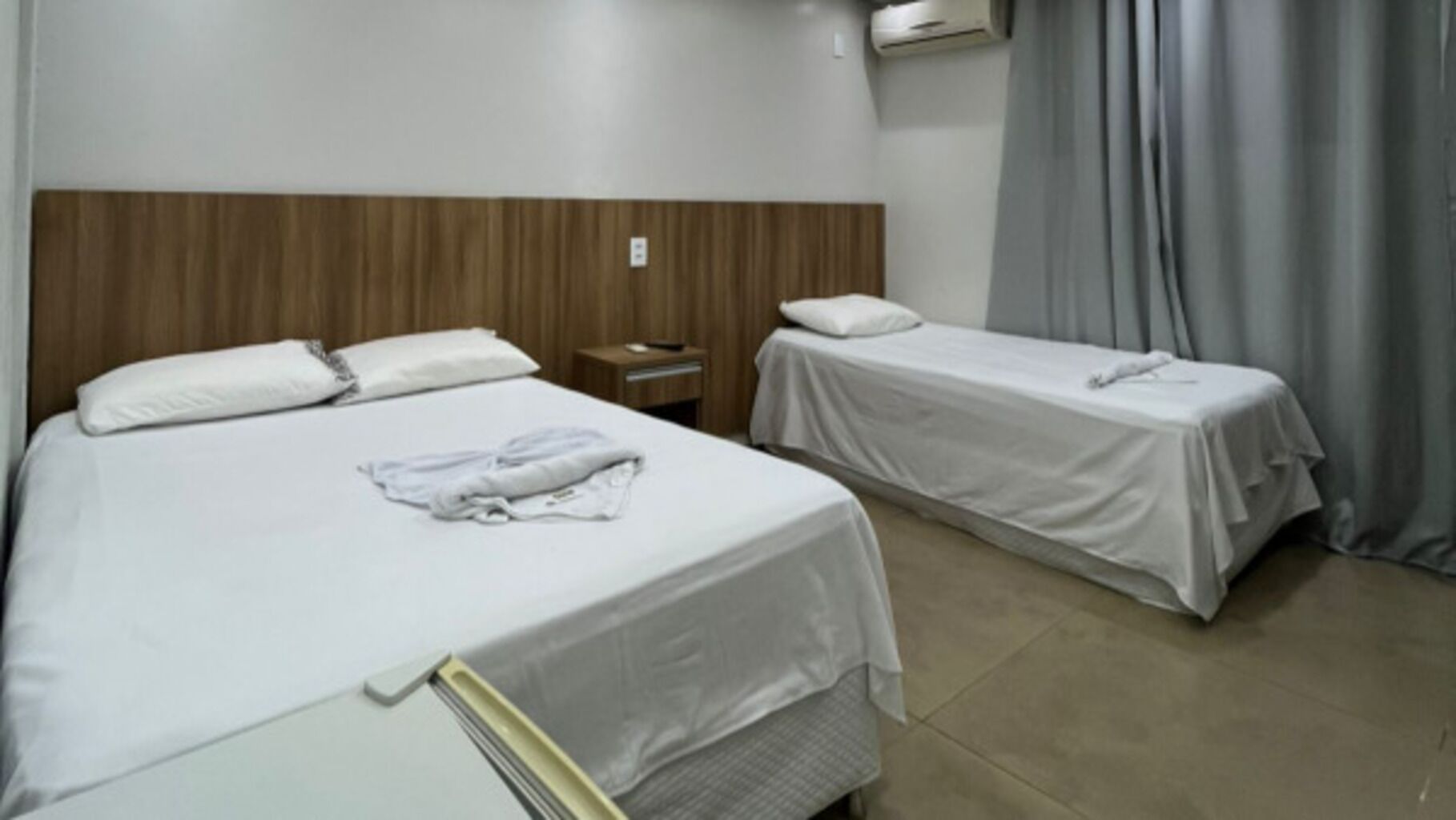 Een hotelkamer met twee eenpersoonsbedden, een houten hoofdbord, een nachtkastje met een lamp en een raam met gordijnen.