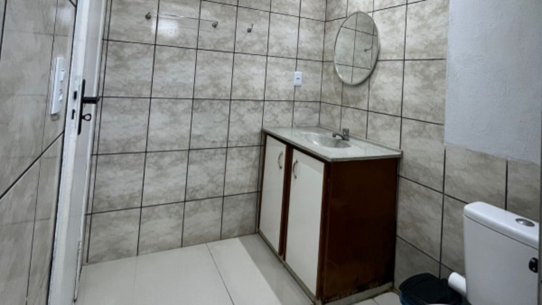 A bathroom with a tiled floor, a sink with a mirror, and a toilet.
