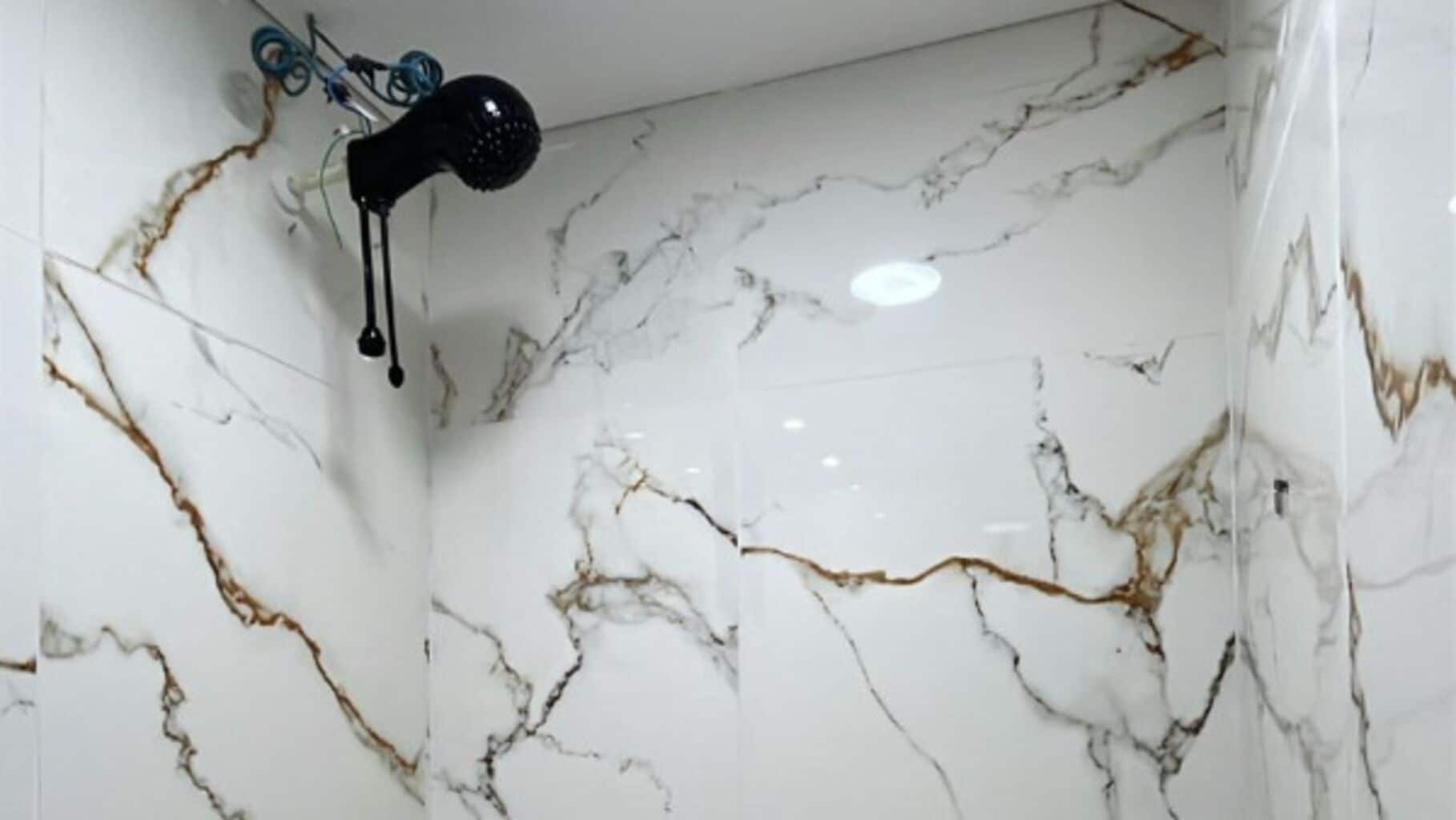 Casa de banho com paredes de mármore branco e secador de cabelo preto fixado na parede.