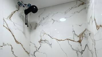 Casa de banho com paredes de mármore branco e secador de cabelo preto fixado na parede.