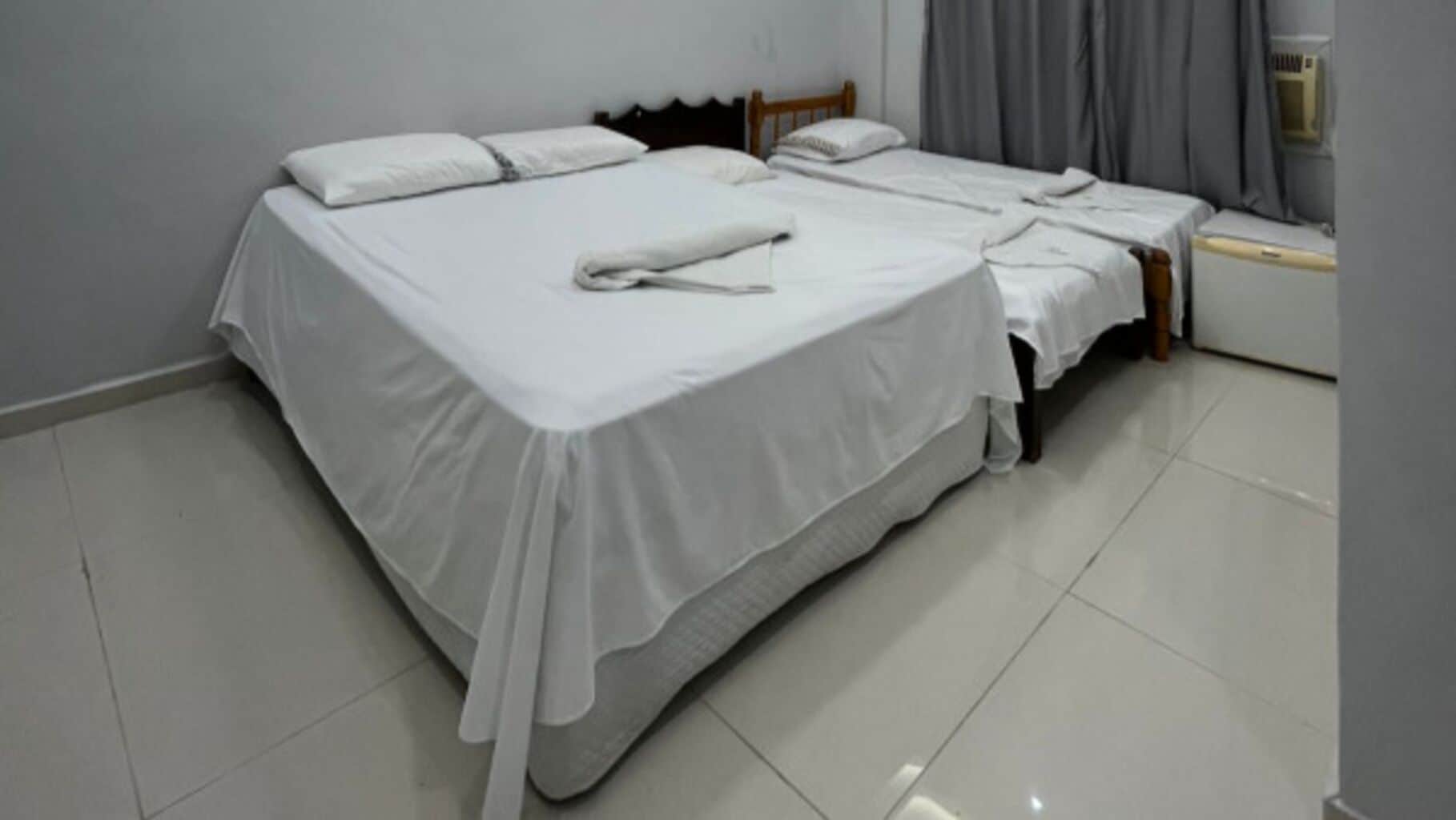 Quarto com duas camas, cada uma com roupa de cama branca e cabeceira de madeira.
