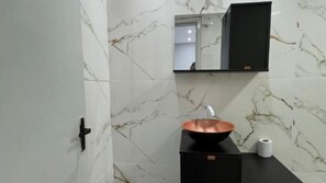 Une salle de bain avec un mur en marbre, un lavabo noir avec un receveur en cuivre, et un meuble noir au-dessus du lavabo.