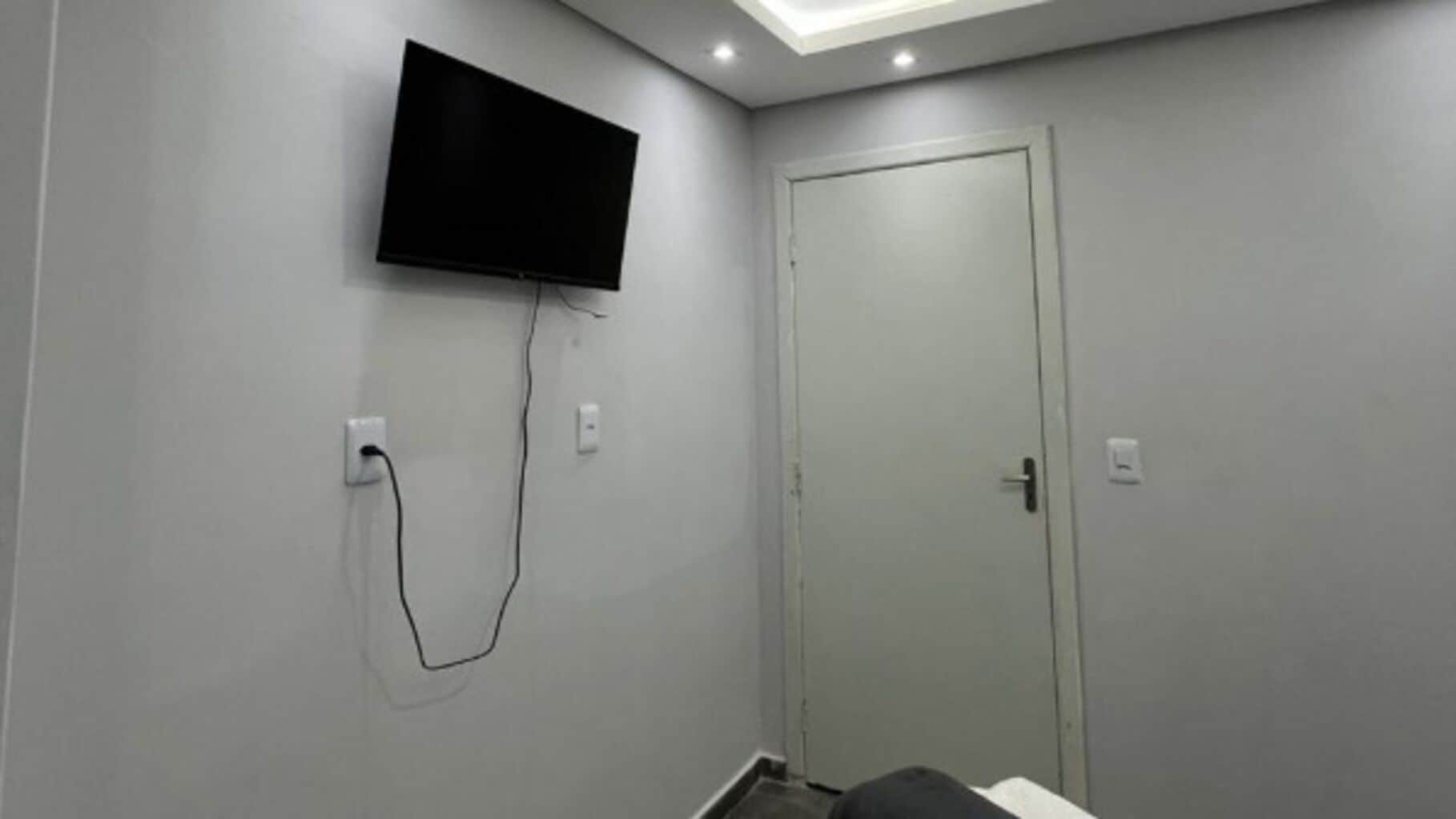 Quarto com televisão de tela plana na parede, uma porta e uma tomada.