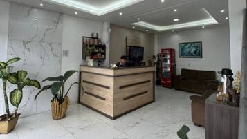 Uma área de recepção moderna com balcão de madeira, máquina de vendas automática vermelha, sofá marrom e plantas em vasos.