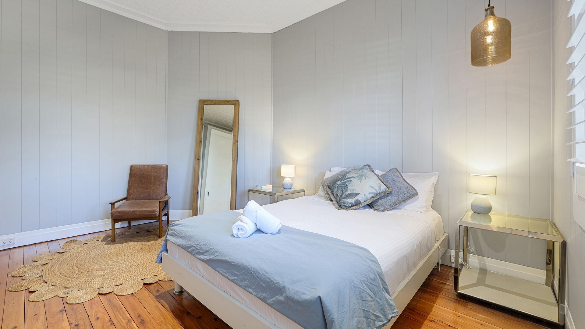 Un dormitorio con una cama, una silla, una mesita de noche con lámpara y un espejo en la pared.