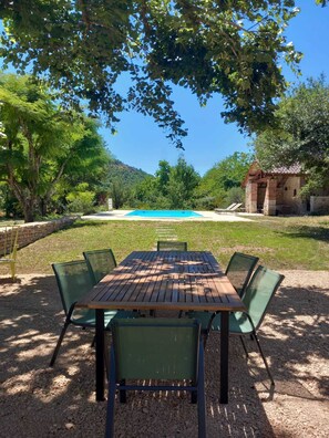 Un tavolo di legno con sedie in un giardino con piscina e un muro in pietra.