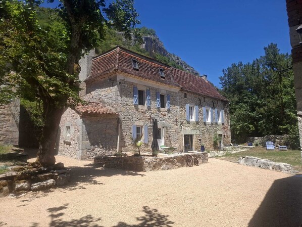 Un edificio in pietra con tetto in tegole rosse, diverse finestre e un cortile in ghiaia.