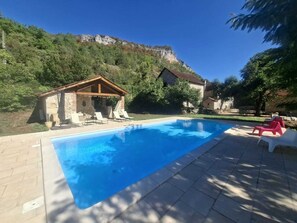 Una piscina con lettini, un edificio in pietra e montagne sullo sfondo.