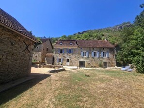 Un edificio in pietra con tetto in tegole, un cortile e una collina sullo sfondo.