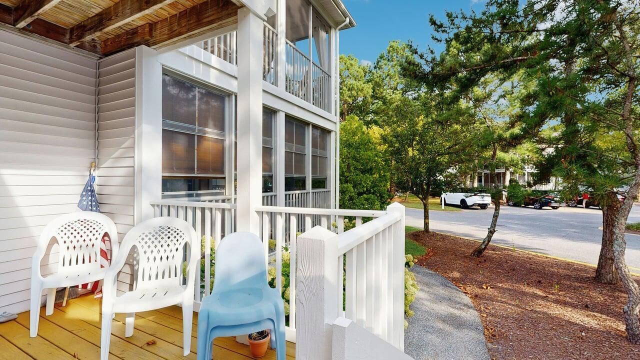A porch with two white plastic chairs, a small potted plant, and a white railing.