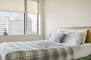 A hotel room with a bed, a window with a view of buildings, and a vase with flowers on the windowsill. - Cozy 1-bedroom apartment Downtown Dallas (Dallas)
