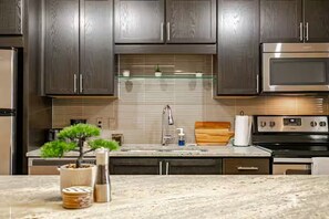 A modern kitchen with dark wood cabinets, stainless steel appliances, a glass shelf, and a granite countertop. - Cozy 1-bedroom apartment Downtown Dallas (Dallas)