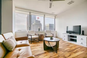 A modern living room with a leather sofa, two armchairs, a coffee table, a TV, and a view of a cityscape through large windows. - Cozy 1-bedroom apartment Downtown Dallas (Dallas)