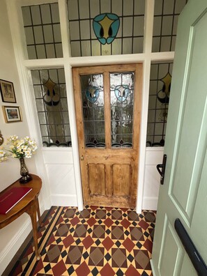 Uma porta de madeira com painéis de vidro, um piso estampado e um vaso com flores.