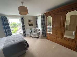 Quarto com cama grande, guarda-roupa de madeira, uma cadeira e janela com cortinas.