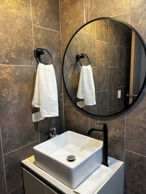 A bathroom with a white sink, a round mirror, and two white towels hanging on hooks. - Vrbo Property (Bogotá)