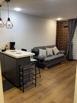A modern living space with a kitchenette, a grey sofa with cushions, a coffee machine, and a brick accent wall. - Vrbo Property (Bogotá)
