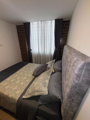 A bedroom with a bed, a window with curtains, and a brick wall. - Vrbo Property (Bogotá)