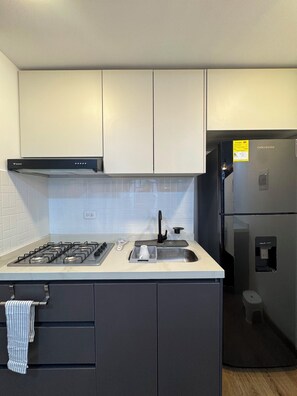 A modern kitchen with a gas stove, stainless steel refrigerator, and white cabinetry. - Vrbo Property (Bogotá)