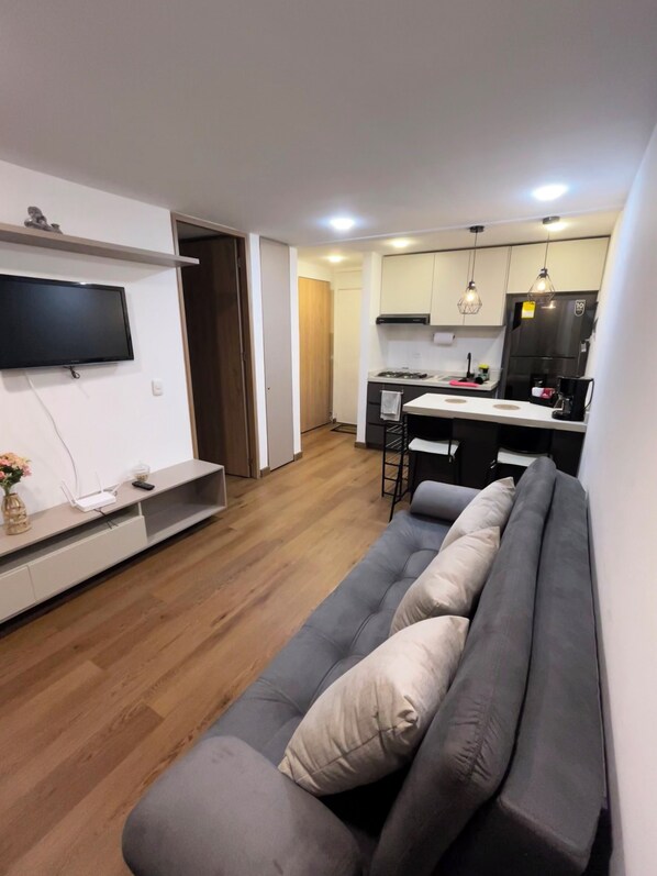 A modern living room with a grey sofa, a flat-screen TV mounted on the wall, and a wooden floor. - Vrbo Property (Bogotá)