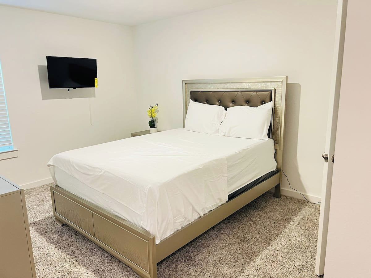 A bedroom with a bed, a nightstand, a TV, and a door.