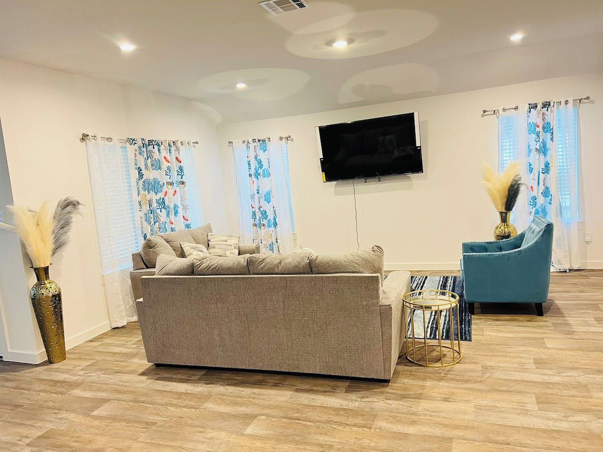 A living room with a sofa, a blue armchair, a flat-screen TV, and decorative vases.