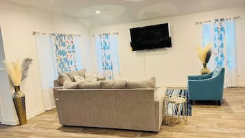 Ein Wohnzimmer mit einer Couch, einem blauen Sessel, einem Flachbildfernseher und dekorativen Vasen.
