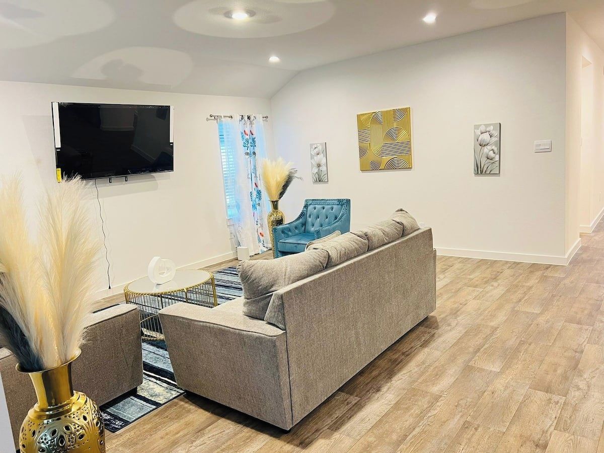 A modern living room with a grey sofa, a blue armchair, and a flat-screen TV mounted on the wall.