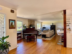 A spacious living room with a grand piano, a fireplace, a sofa, and a dining area with chairs.