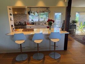 Una cocina moderna con una isla central, tres taburetes altos y vistas al exterior.