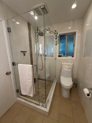 Un baño moderno con ducha envuelta en vidrio, inodoro y ventana.
