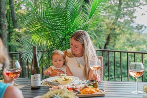 A woman and a child dining at an outdoor table with a bottle of wine and a glass of wine. - Melrose's Place | Mountain Views + Hot Tub (Tryon)