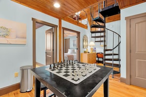 A spacious room with a large chessboard, a staircase, and a bed in the background. - Melrose's Place | Mountain Views + Hot Tub (Tryon)