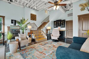 A spacious living area with a staircase, a large window, and a ceiling fan. - Melrose's Place | Mountain Views + Hot Tub (Tryon)