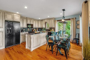 A spacious kitchen with a large island, wooden flooring, and a dining area with chairs and a table. - Melrose's Place | Mountain Views + Hot Tub (Tryon)