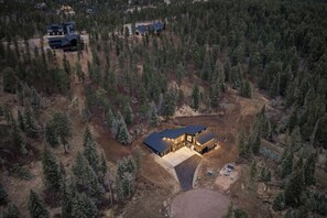 A large, multi-story lodge surrounded by dense forest, with a well-lit driveway leading to the entrance. - Top Shelf Lodge -luxury 6 bedroom 6.5 bathroom AC, Hot Tub, Golf Simulato (Lead)