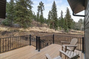 A wooden deck with a black metal railing, surrounded by a forested area. - Top Shelf Lodge -luxury 6 bedroom 6.5 bathroom AC, Hot Tub, Golf Simulato (Lead)