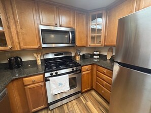 Cocina con armarios de madera y electrodomésticos de acero inoxidable, incluyendo microondas, estufa, horno y refrigerador.