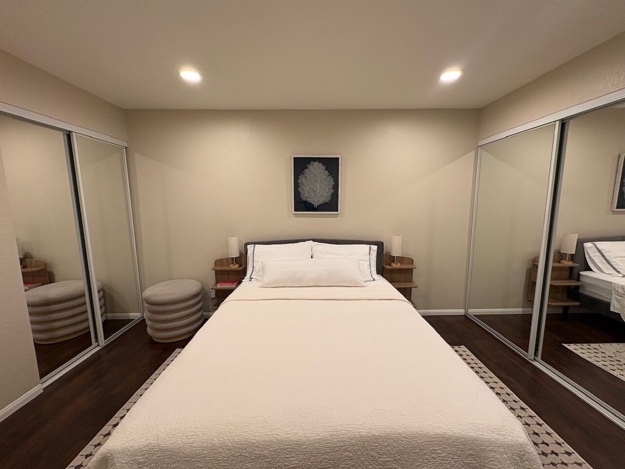 A hotel room with a bed, bedside tables, a mirror, and a framed artwork on the wall.