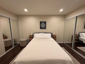 Ein Hotelzimmer mit Bett, Nachttischen, einem Spiegel und einem gerahmten Kunstwerk an der Wand.