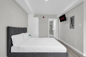 A modern bedroom with a large bed, a flat-screen TV mounted on the wall, and a visible door leading to a bathroom.