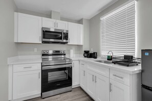 A modern kitchen with white cabinetry, a stainless steel oven, a microwave, and a built-in sink.