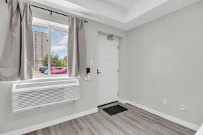 A room with a window, a door, a radiator, and a black mat on the floor.