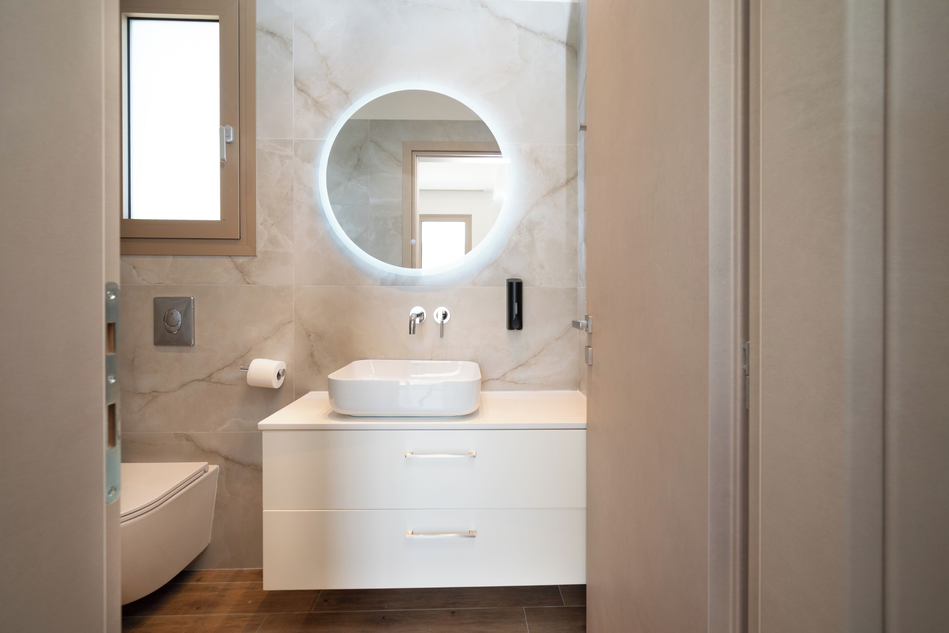 Un bagno moderno con uno specchio rotondo, un lavandino bianco e un water.