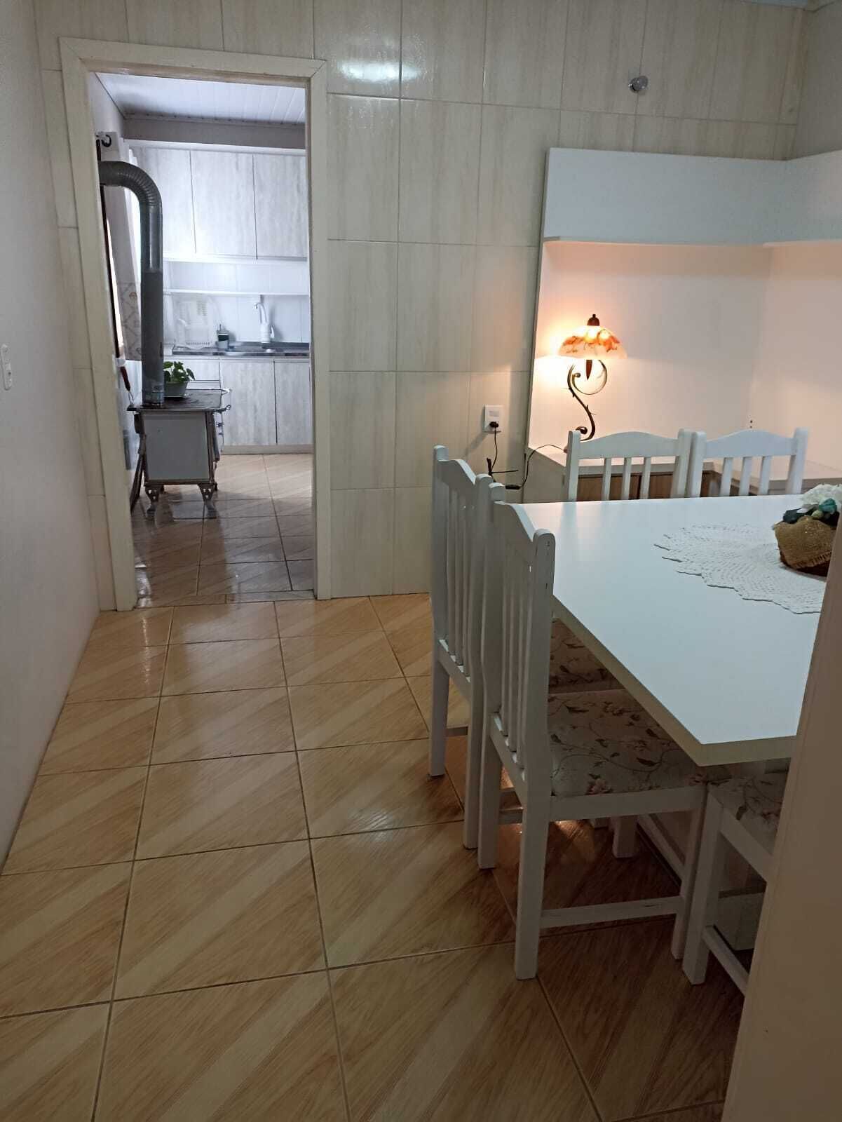 A dining area with a white table and chairs, a small kitchen in the background, and a hallway leading to another room.