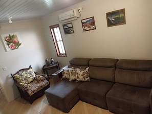 Ein Wohnzimmer mit einem braunen Sofa, einem blumigen Sessel und einem kleinen Tisch mit Dekoration. An der Wand befinden sich drei gerahmte Bilder.